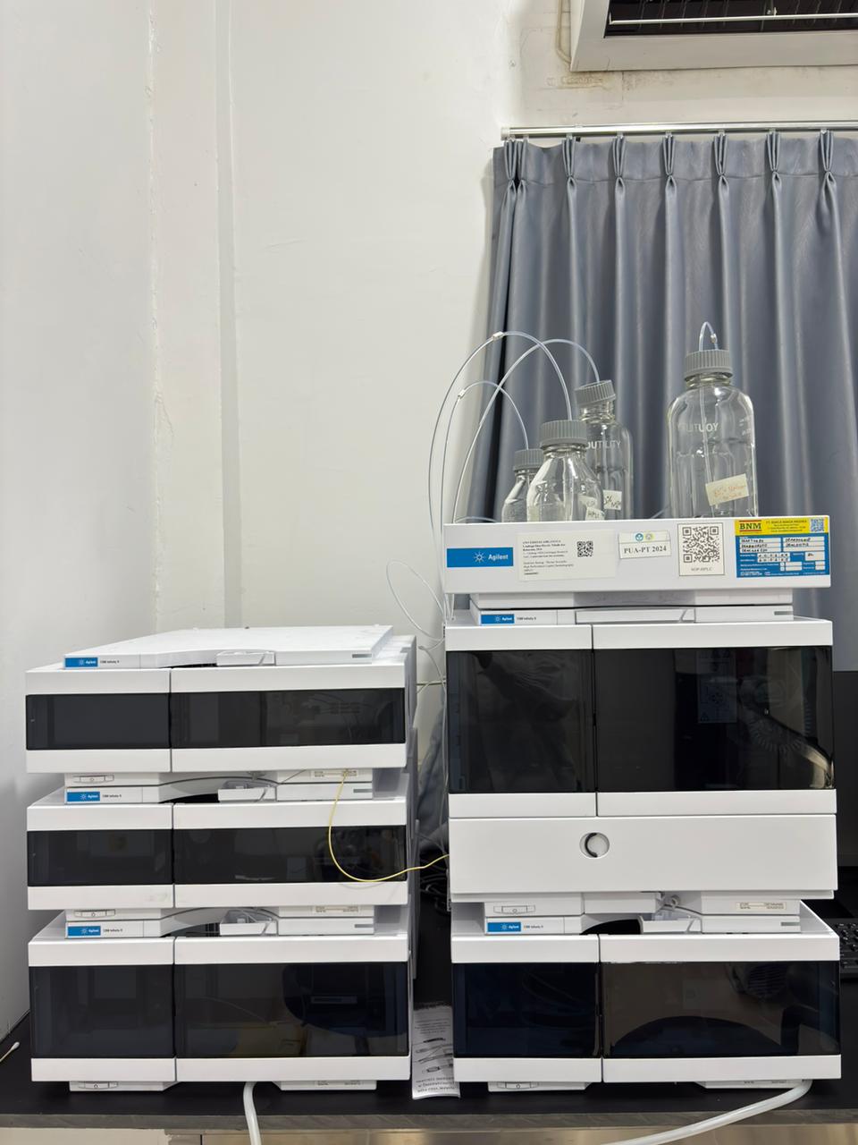 Peralatan High Performance Liquid Chromatography (HPLC) Agilent yang terdiri dari unit pemroses data di sebelah kiri dan autosampler dengan botol-botol sampel kaca di sebelah kanan, menunjukkan sistem analitik modern untuk pemisahan dan identifikasi sampel kimia